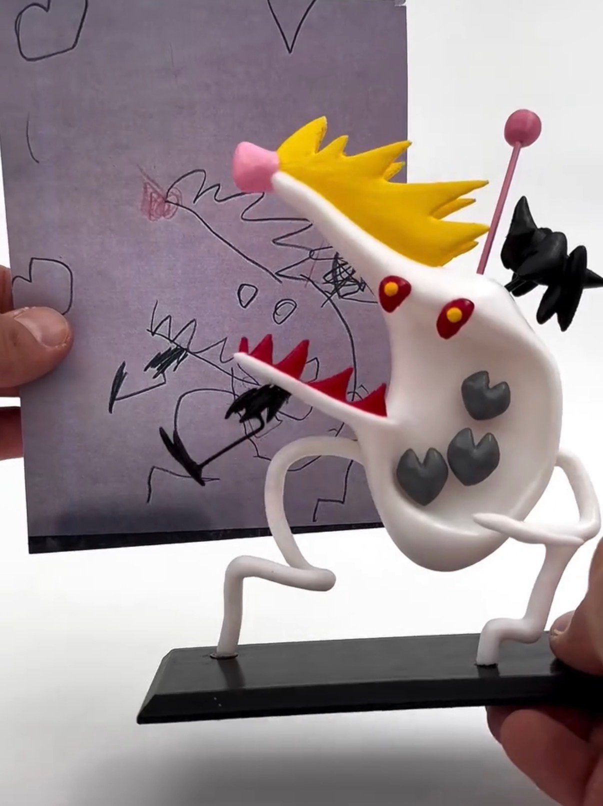 A white monster figurine with a yellow crown held beside its original scribbled drawing